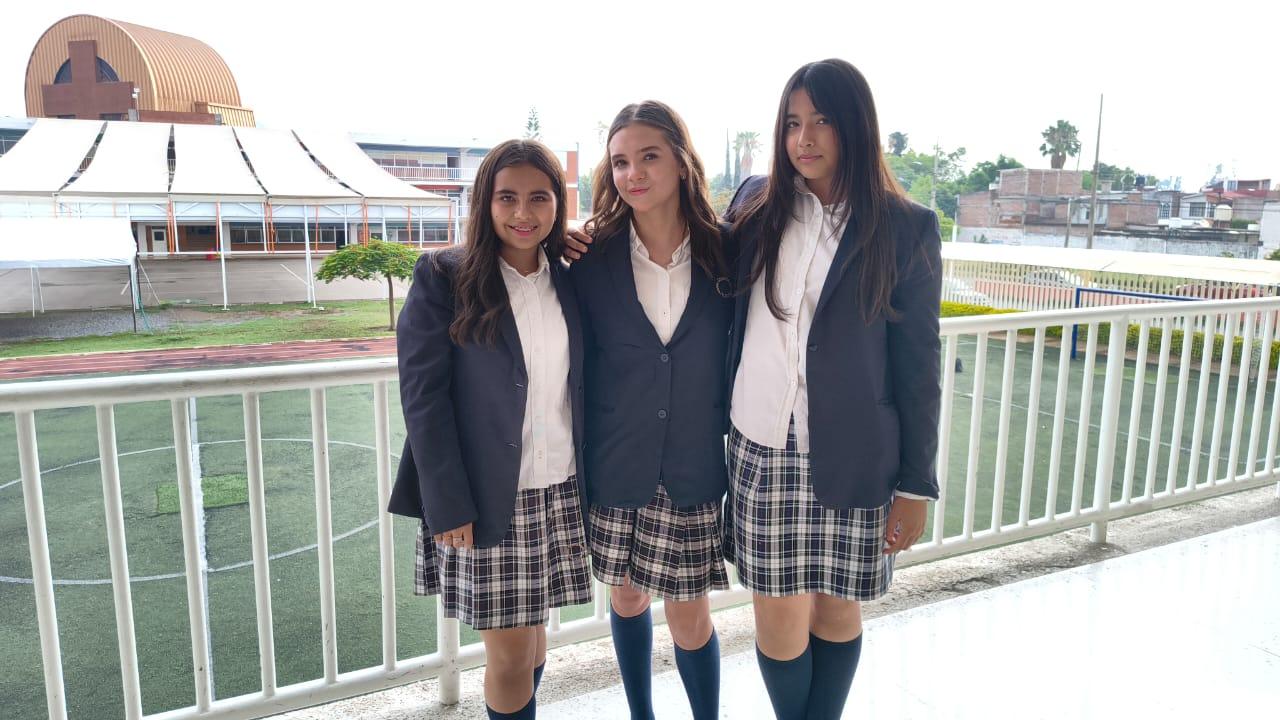 Tres estudiantes con uniforme escolar posando en instalaciones del colegio junto a campo deportivo